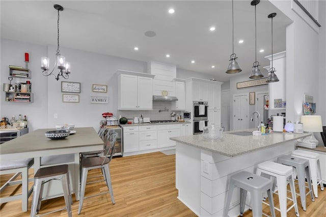 1033 Lanier Ave, Gainesville, GA 30501 - kitchen featuring decorative backsplash, white cabinets, stainless steel double oven, light wood-style floors, and a sink