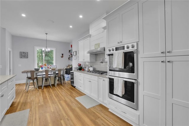 1033 Lanier Ave, Gainesville, GA 30501 - kitchen with light wood finished floors, white cabinets, decorative backsplash, appliances with stainless steel finishes, and a notable chandelier