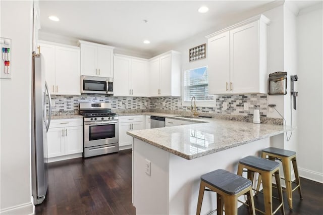 kitchen with stainless steel appliances, dark wood-type flooring, a sink, and a peninsula