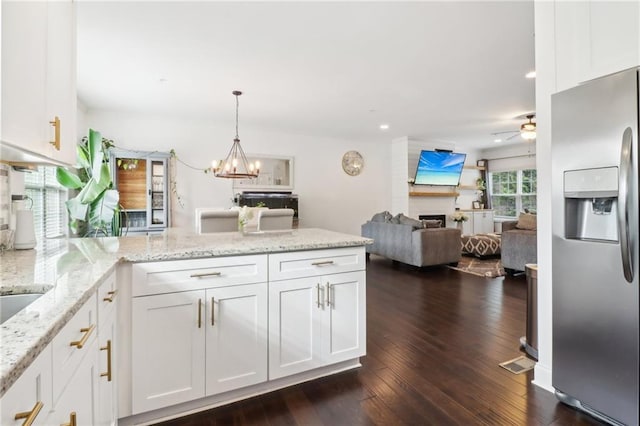 kitchen with a peninsula, a fireplace, white cabinetry, open floor plan, and stainless steel refrigerator with ice dispenser