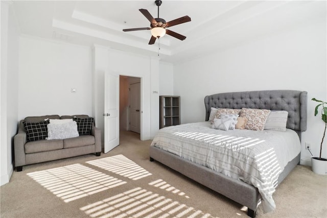 carpeted bedroom with a raised ceiling and a ceiling fan