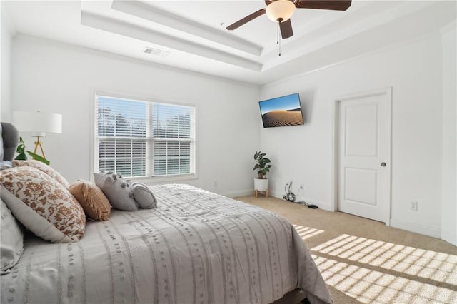 carpeted bedroom with a ceiling fan, a tray ceiling, visible vents, and baseboards