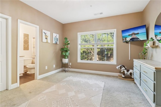 interior space with light carpet, visible vents, baseboards, and ensuite bathroom