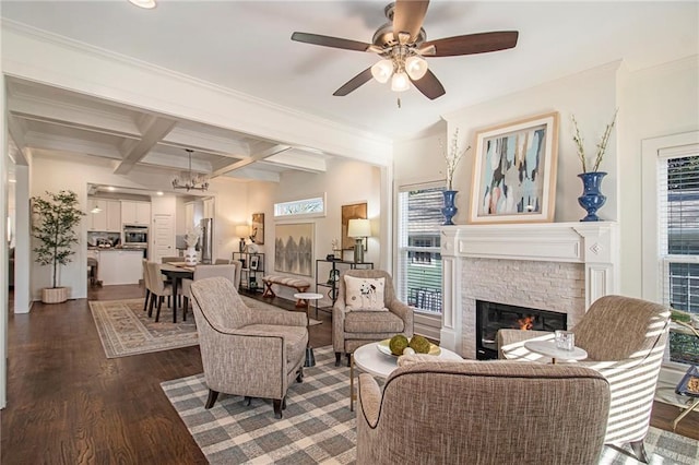 living room with beamed ceiling, ceiling fan with notable chandelier, coffered ceiling, dark wood finished floors, and a stone fireplace