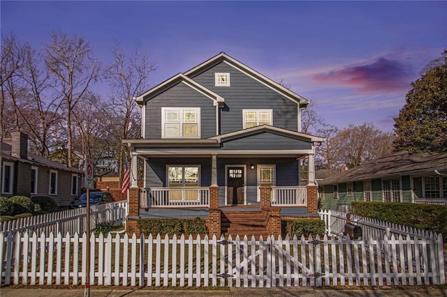 view of front facade featuring brick siding, covered porch, and a fenced front yard