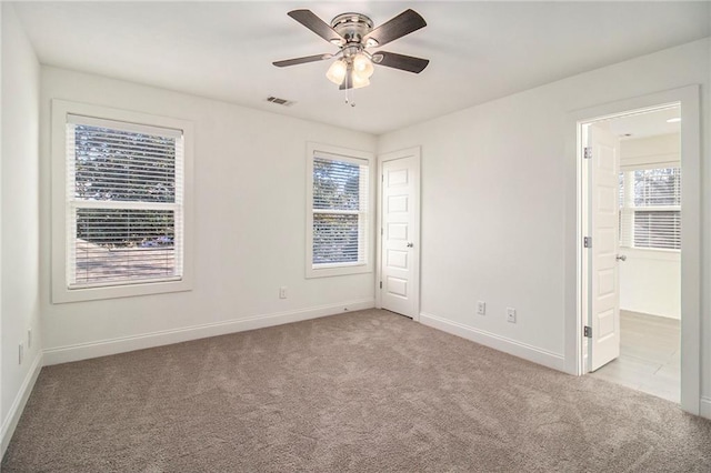 unfurnished room featuring light carpet, visible vents, baseboards, and ceiling fan