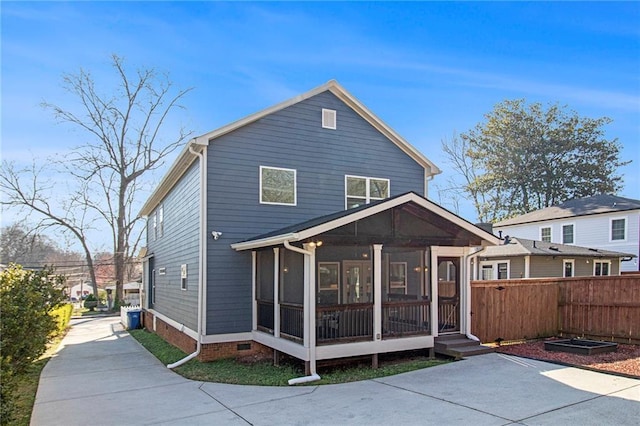 rear view of property with concrete driveway, fence, and a sunroom