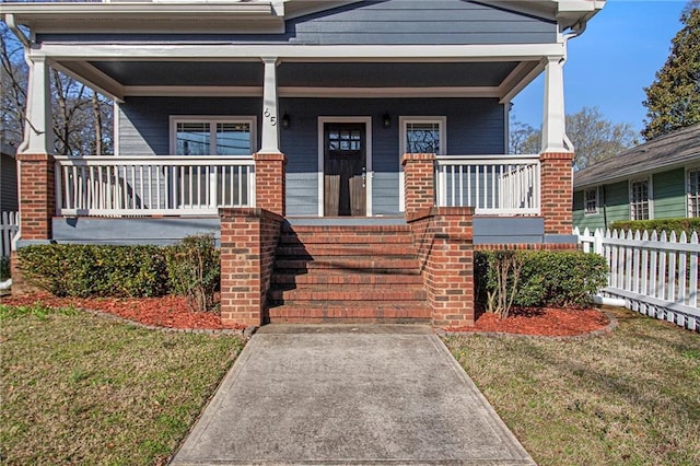 entrance to property with a yard, covered porch, and fence