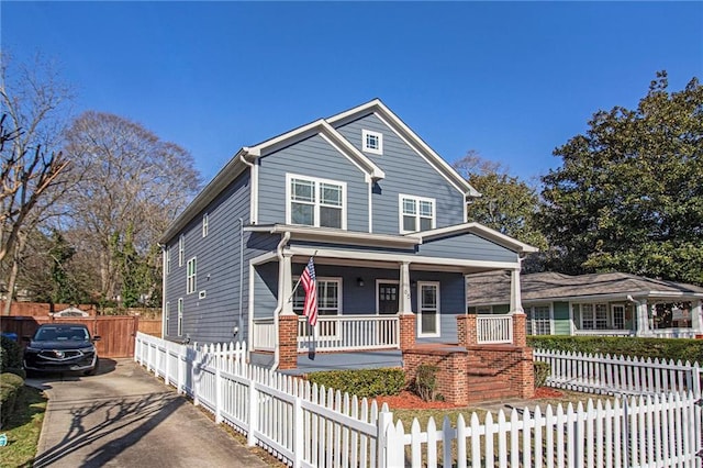 view of front of house with a fenced front yard, covered porch, driveway, and brick siding