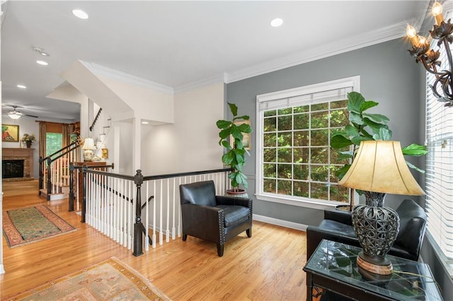 living area with wood finished floors, ornamental molding, a fireplace, ceiling fan, and baseboards