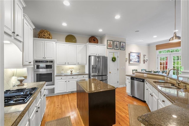 kitchen featuring a center island, ornamental molding, a sink, white cabinets, and appliances with stainless steel finishes