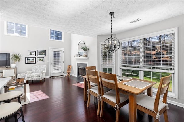 dining room featuring visible vents, a fireplace, dark wood-style floors, a notable chandelier, and a textured ceiling