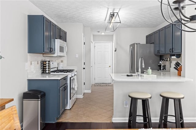 kitchen with a kitchen breakfast bar, white appliances, a peninsula, light countertops, and decorative backsplash