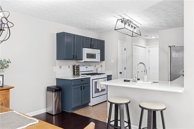 kitchen featuring a kitchen bar, light countertops, a peninsula, white appliances, and blue cabinets