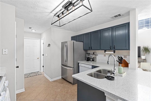 kitchen featuring visible vents, light stone counters, freestanding refrigerator, white dishwasher, and a sink