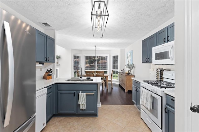 kitchen with a sink, blue cabinetry, white appliances, a peninsula, and light countertops