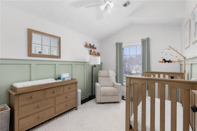 bedroom featuring visible vents, a wainscoted wall, light colored carpet, lofted ceiling, and a nursery area