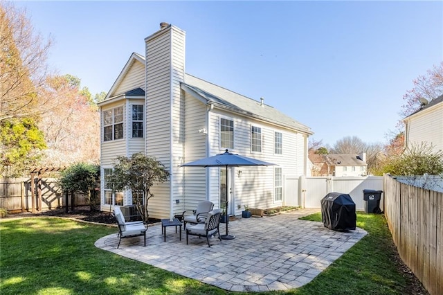 back of house with a yard, a fenced backyard, a chimney, and a patio area