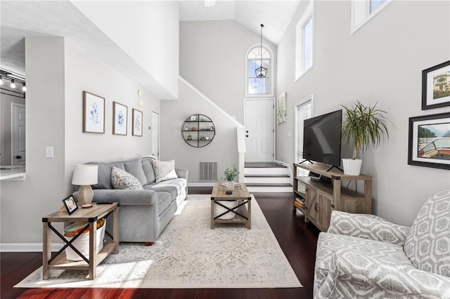 living room featuring dark wood finished floors, visible vents, high vaulted ceiling, and stairs