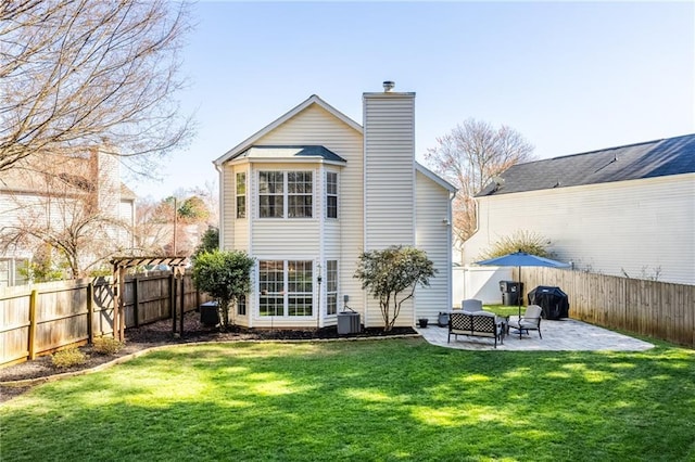 back of house featuring central air condition unit, a chimney, a fenced backyard, a yard, and a patio area