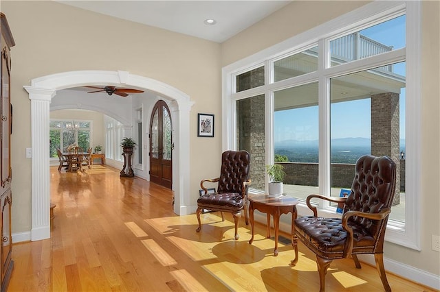 living area with a mountain view, light hardwood / wood-style flooring, decorative columns, and ceiling fan