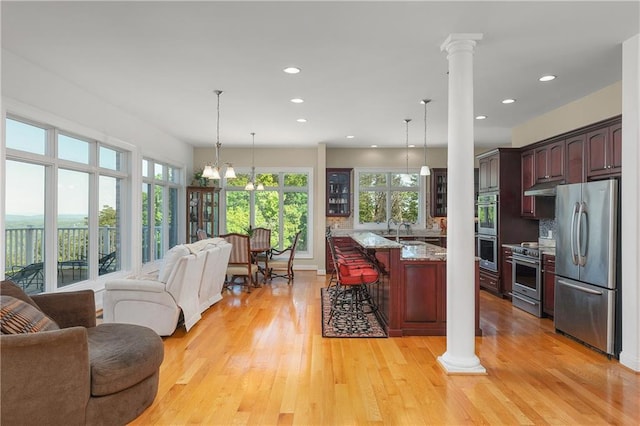 kitchen with stainless steel appliances, a kitchen breakfast bar, light hardwood / wood-style floors, light stone countertops, and ornate columns