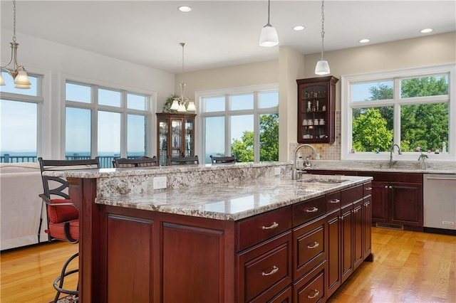 kitchen featuring sink, decorative light fixtures, stainless steel dishwasher, a kitchen breakfast bar, and an island with sink