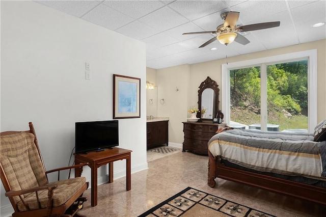 bedroom featuring ceiling fan, connected bathroom, and a drop ceiling