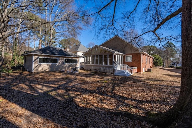 rear view of property featuring a sunroom, brick siding, and an outbuilding