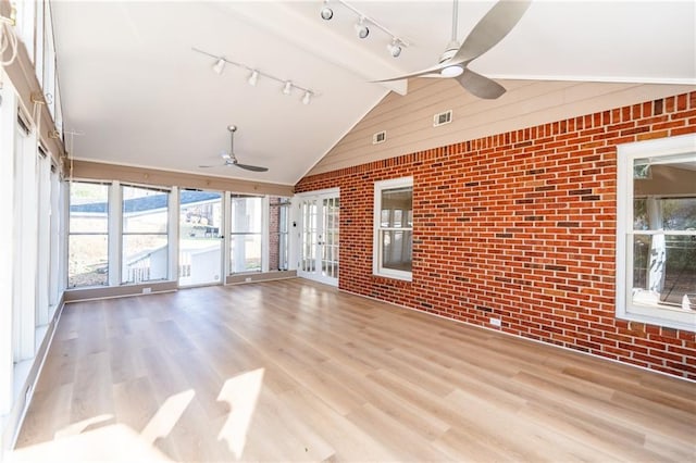 interior space with a ceiling fan, vaulted ceiling, brick wall, and wood finished floors