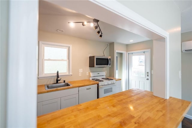 kitchen with white appliances, a sink, white cabinetry, wooden counters, and an AC wall unit