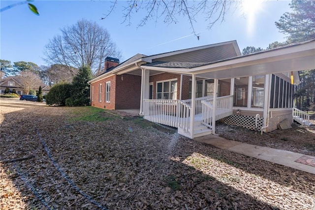 view of side of property featuring brick siding, a chimney, and a sunroom