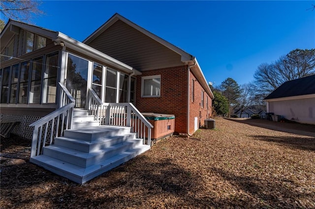 back of property featuring a sunroom, brick siding, and central AC unit