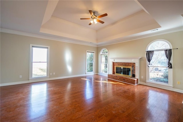 unfurnished living room featuring plenty of natural light, a fireplace, a tray ceiling, and wood finished floors