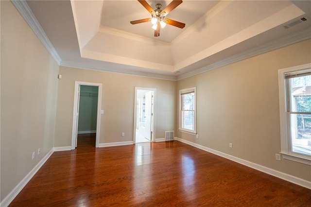 spare room featuring dark wood-style flooring, crown molding, a raised ceiling, visible vents, and baseboards