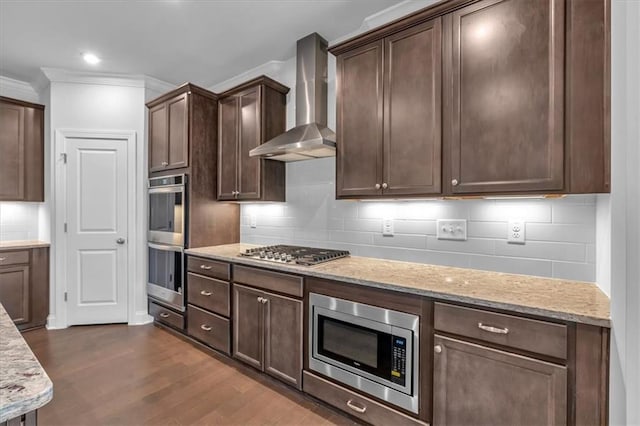 kitchen featuring dark hardwood / wood-style flooring, ornamental molding, light stone counters, stainless steel appliances, and wall chimney exhaust hood