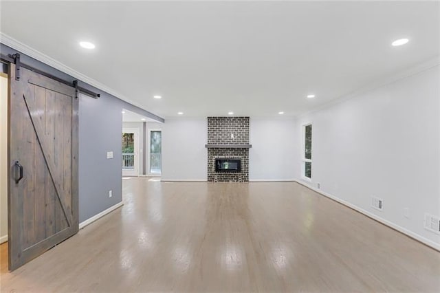 unfurnished living room featuring light wood finished floors, a fireplace, crown molding, and a barn door