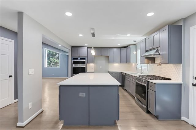 kitchen with under cabinet range hood, stainless steel appliances, gray cabinets, and a sink