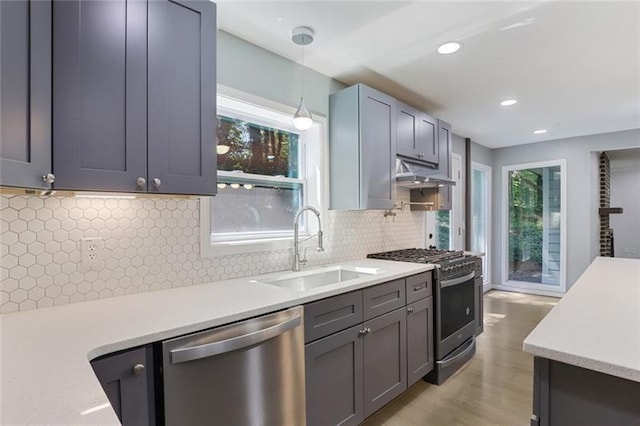 kitchen featuring under cabinet range hood, light countertops, hanging light fixtures, stainless steel appliances, and a sink