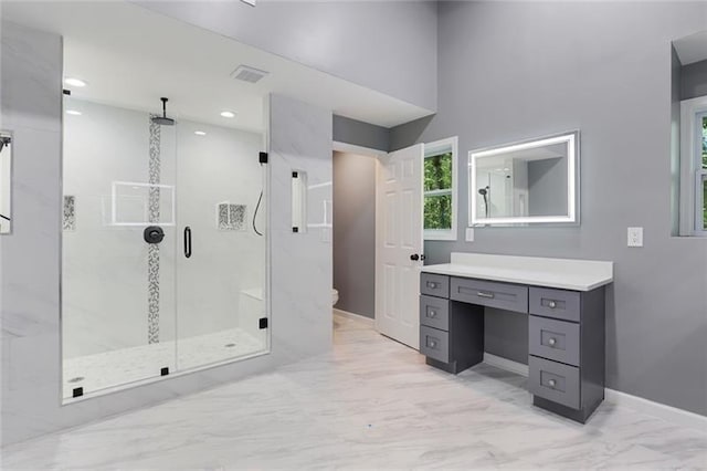 bathroom featuring toilet, marble finish floor, a shower stall, baseboards, and vanity