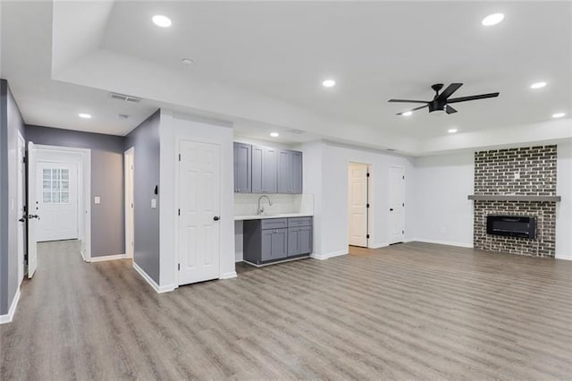 unfurnished living room featuring recessed lighting, a fireplace, wood finished floors, a ceiling fan, and a sink