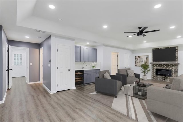 living area featuring a raised ceiling, a brick fireplace, recessed lighting, and light wood-style floors