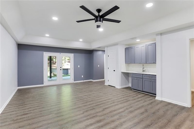 unfurnished living room featuring ceiling fan, a raised ceiling, wood finished floors, and recessed lighting