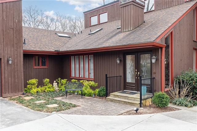 view of exterior entry featuring french doors and roof with shingles