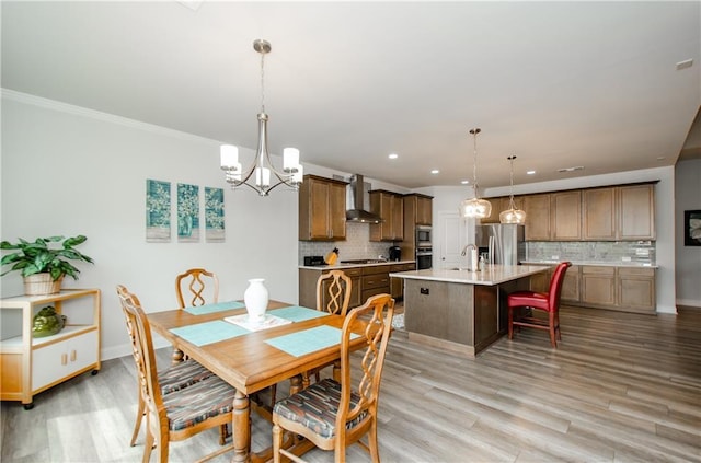 dining space with crown molding, sink, a chandelier, and light hardwood / wood-style floors