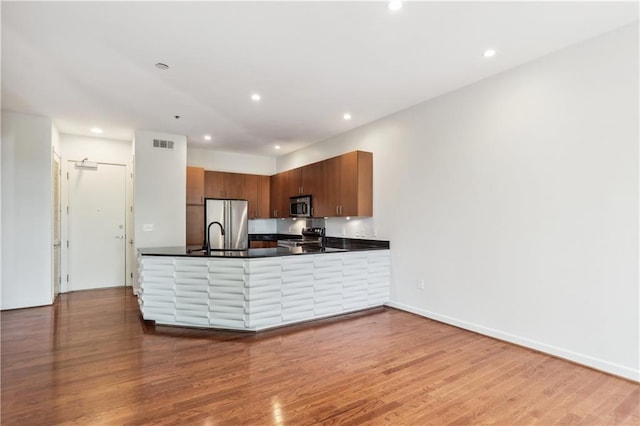 kitchen with wood-type flooring, kitchen peninsula, and stainless steel appliances