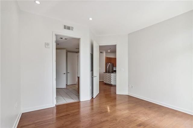 unfurnished bedroom with stainless steel fridge and hardwood / wood-style floors