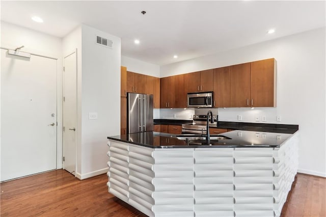 kitchen featuring appliances with stainless steel finishes, hardwood / wood-style flooring, kitchen peninsula, and sink