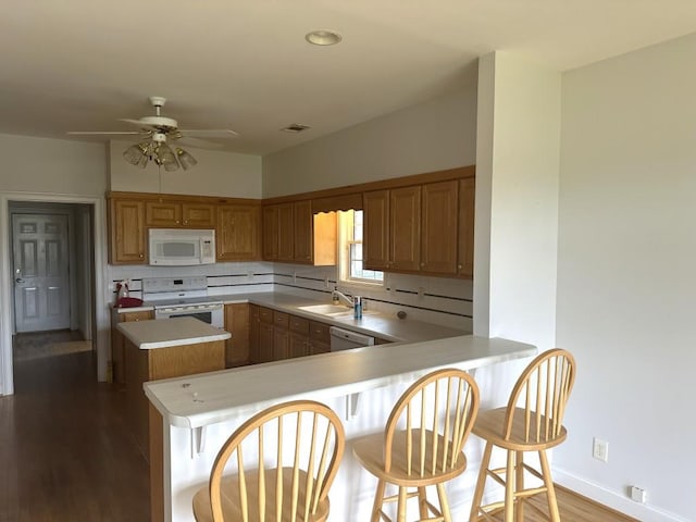 kitchen featuring brown cabinets, tasteful backsplash, light countertops, white appliances, and a peninsula