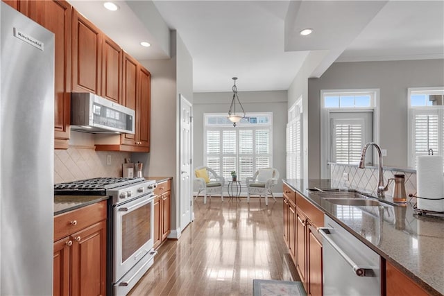 kitchen featuring dark stone countertops, hanging light fixtures, light hardwood / wood-style flooring, stainless steel appliances, and sink